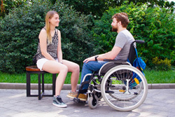 BIldinhalt: ein junger Mann im Rollstuhl unterhält sich mit einer jungen Frau